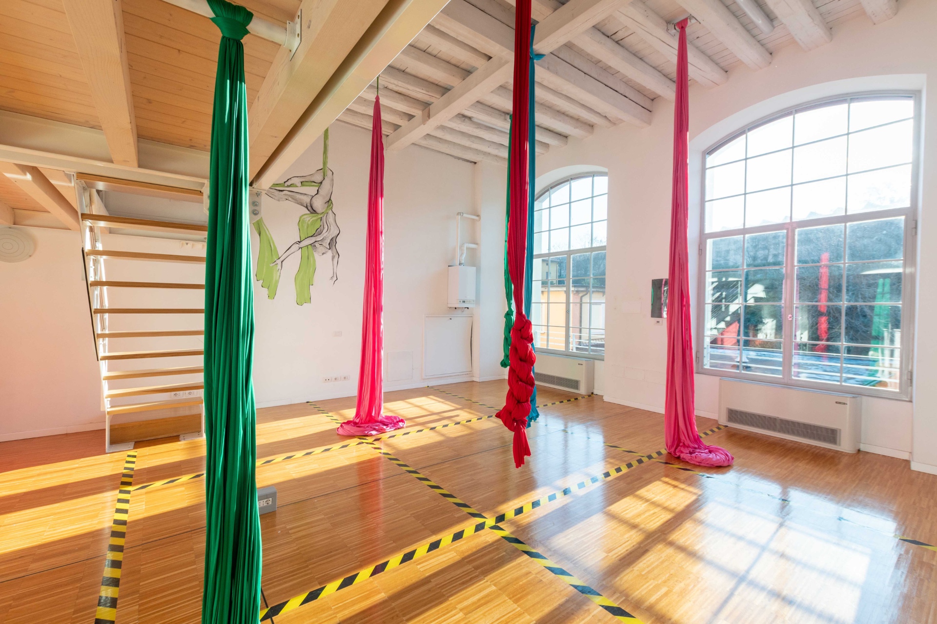 La sala di Officina Dadà con i tessuti aerei colorati appesi al soffitto in legno